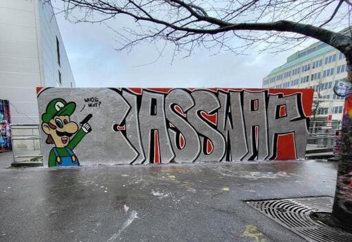 A graffiti mural with the text "Class War", a cartoon drawing of Luigi the Plumber holding a pistol to the side, happily asking us "Who's next?"